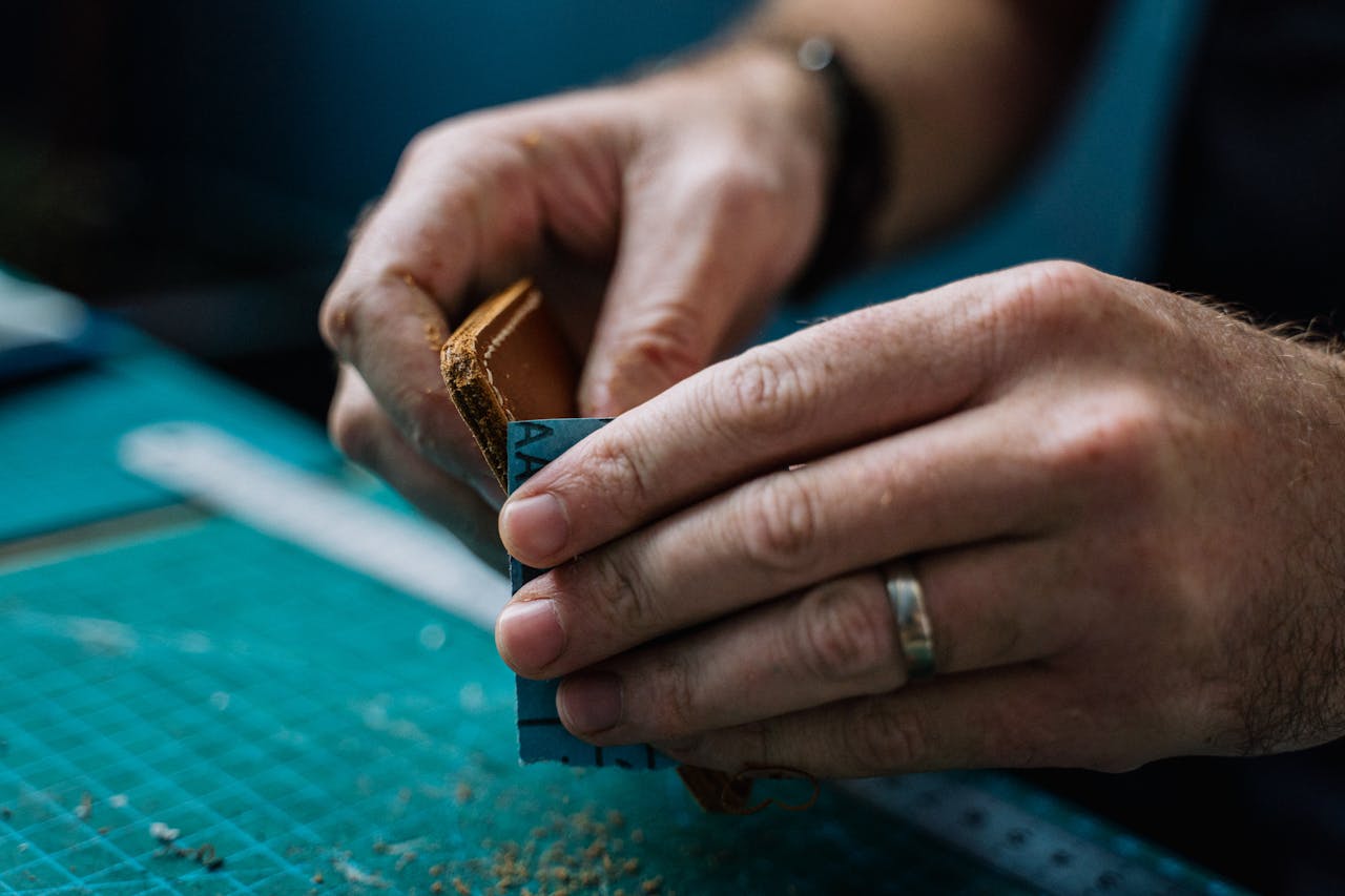 why-choose-us Close-up of skilled craftsman hands sanding a handmade leather wallet, showcasing fine craftsmanship and attention to detail.